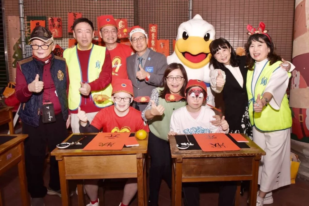 圖／副市長林奕華逛園遊會，於總監林振邦、活動主委金文徵及華朋扶輪社吉祥物「朋鵬」陪同下，在「逸鵝書屋」書法攤揮毫。（松山社區大學 提供）