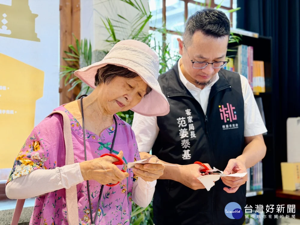 客家局長范姜泰基(右)及李南華女士(左)共同體驗漢聲雜誌曾介紹的剪紙藝術，現場剪出聖蹟亭的剪影。